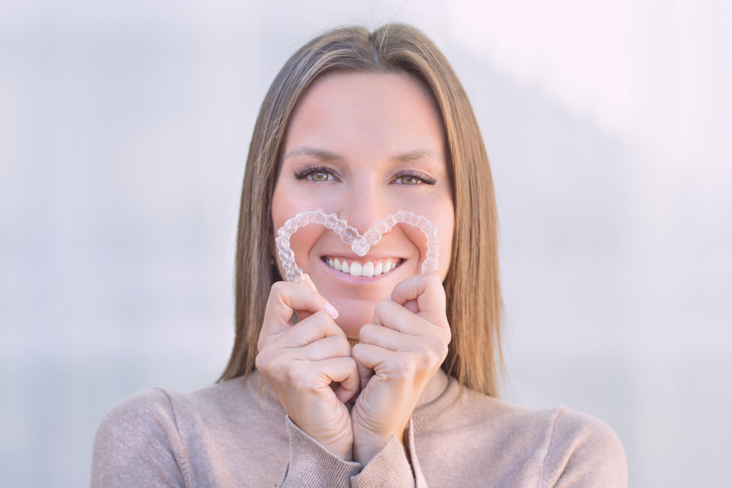 woman holding two clear aligners in a heart shape